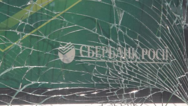 Рабочие собирали осколки выбитых взрывом стекол отделения Сбербанка РФ в Киеве