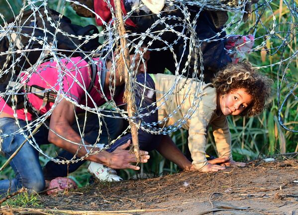 Мигранты проползают под колючей проволокой на Венгерско-Сербской границе