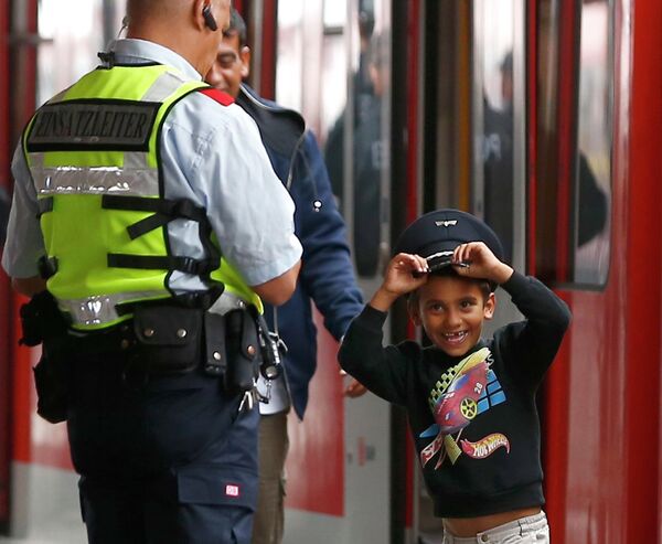 Мальчик из семьи мигрантов в фуражке сотрудника безопасности железной дороги Германии на станции в Мюнхене