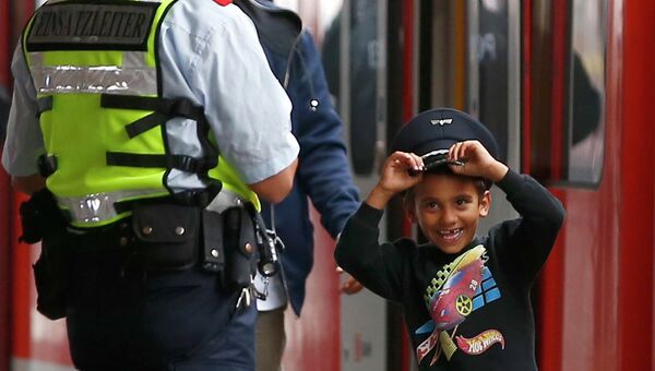 Мальчик из семьи мигрантов в фуражке сотрудника безопасности железной дороги Германии на станции в Мюнхене