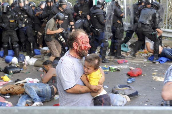 Мужчина с ребенком, пострадавший во время столкновения с полицией на границе Венгрии и Сербии. 16 сентября 2015
