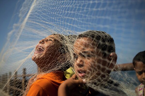 Палестинские дети играют с рыболовной сетью на пляже в Газе