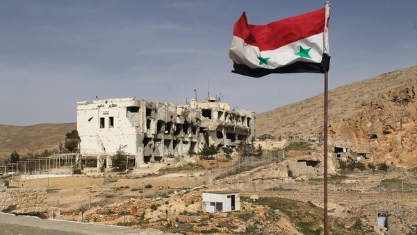 Сирийский флаг на фоне разрушенного дома в сирийском городе Маалюля в 55 км от Дамаска, который дважды захватывали и грабили боевики из группировки Джабхат ан-Нусра