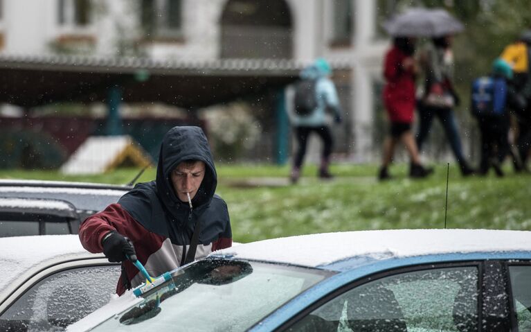 Молодой человек очищает свой автомобиль от снега в одном из дворов в Новокосино, Москва