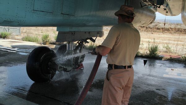 Техник поливает шасси российского самолета, чтобы остудить после приземления на авиабазе Хмеймим, Сирия