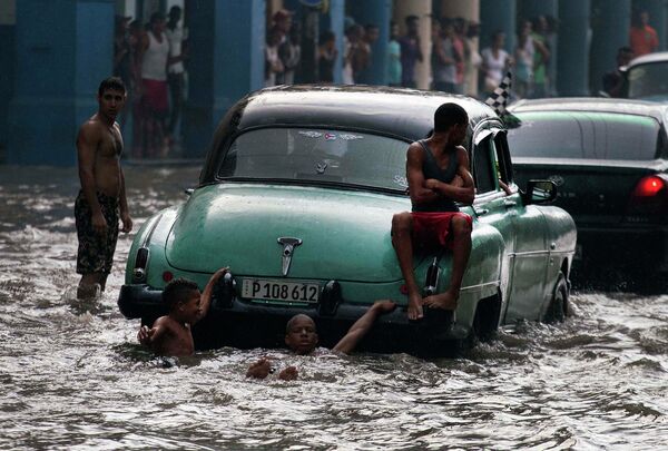 Жители Гаваны висят на бампере старинных автомобилей на затопленной улице. Куба, октябрь 2015