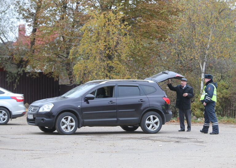 Сотрудник ДПС досматривает машину автовладельца на одной из улиц деревни Тимошкино