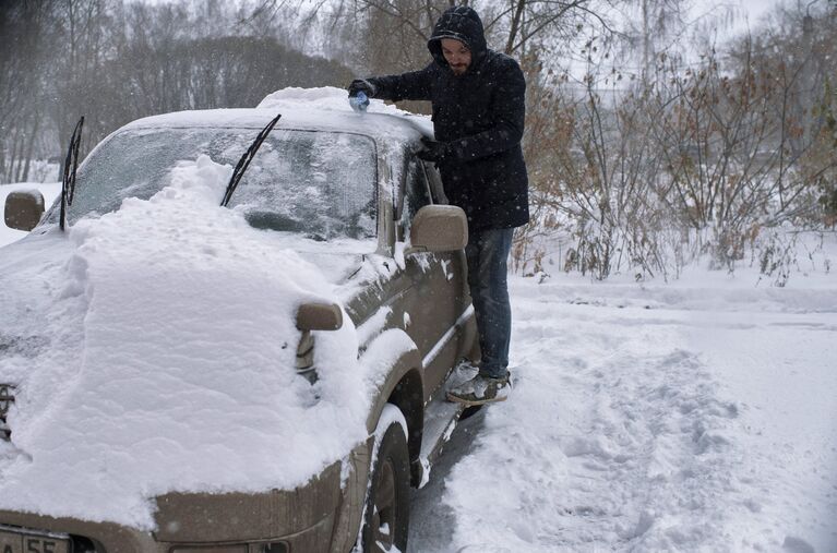 Мужчина чистит автомобиль во время сильного снегопада на одной из улиц города Омска