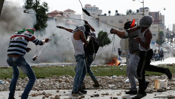 Палестинские демонстранты кидают камни в направлении израильских сил безопасности на окраине Рамаллы. Октябрь 2015