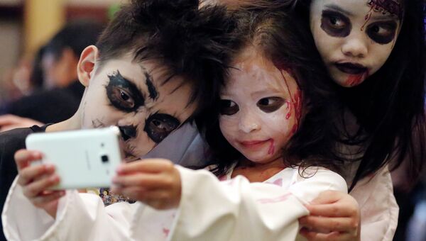 Загримированные дети фотографируются на телефон в канун Хэллоуина. Архивное фото
