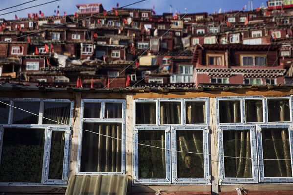 Буддистский монах смотрит из окна своего жилища неподалеку от института буддизма Ларунг Гар, Тибетский автономный район, КНР