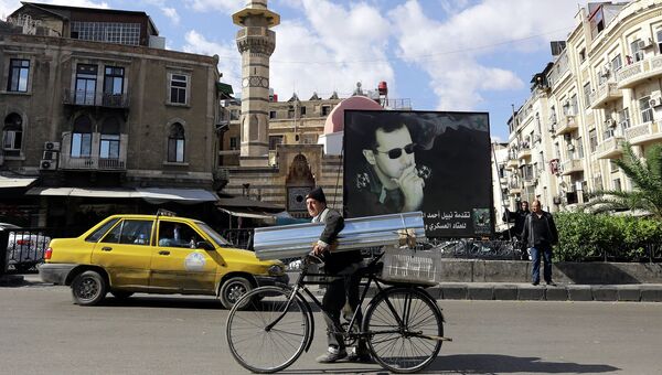 Житель Сирии на улице Дамаска в Сирии на фоне баннера с изображением президента Сирии Башара Асада. Ноябрь 2010