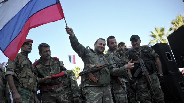 Сирийские военные с российским флагом во время митинга в городе Тартус, Сирия
