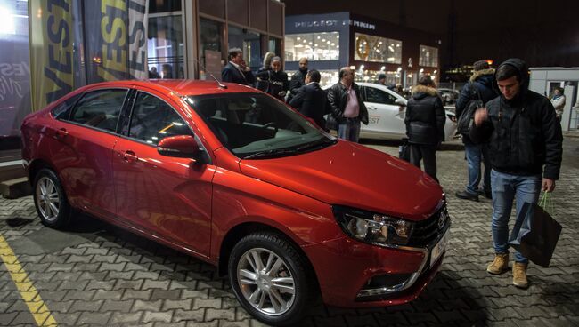 Молодые люди осматривают автомобиль Lada Vesta после начала продаж в Москве. Архивное фото