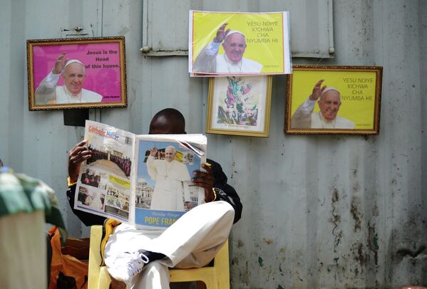 Мужчина читает газету Catholic Mirror на фоне портретов Папы Римского в Найроби, Кения