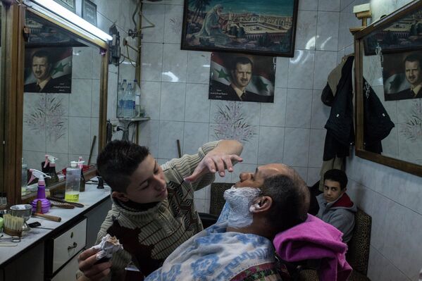 Парикмахер бреет клиента в одной из парикмахерских в Дамаске