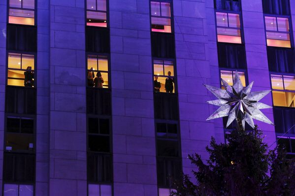 Офисные работники наблюдают за церемонией зажжения огней главной рождественской елки у небоскреба Рокфеллер-центра в Нью-Йорке, США