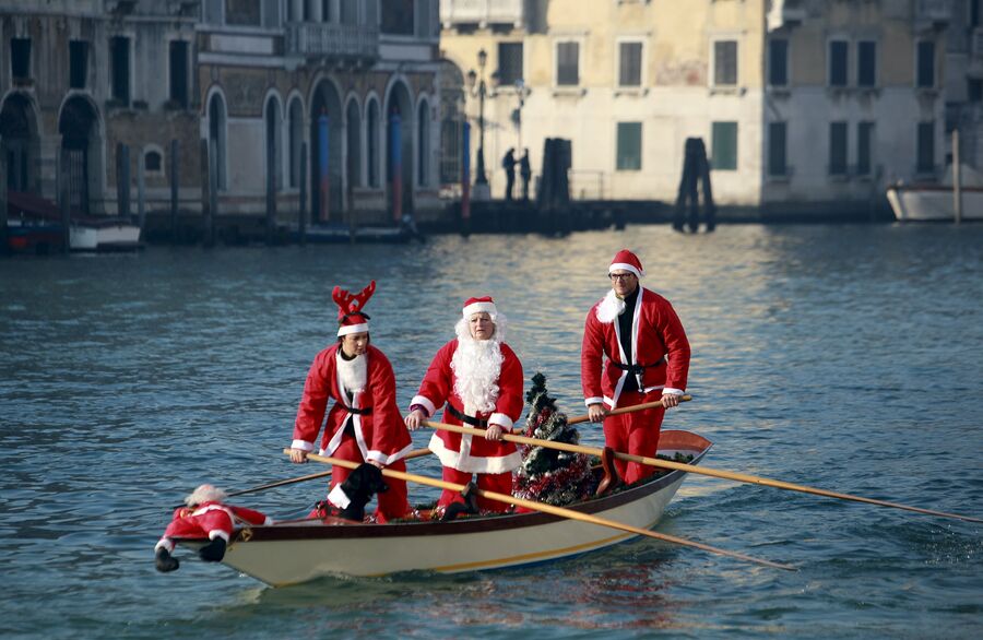 Люди, одетые в костюмы Санта-Клаусов, плывут на лодке по Гранд-каналу, Венеция