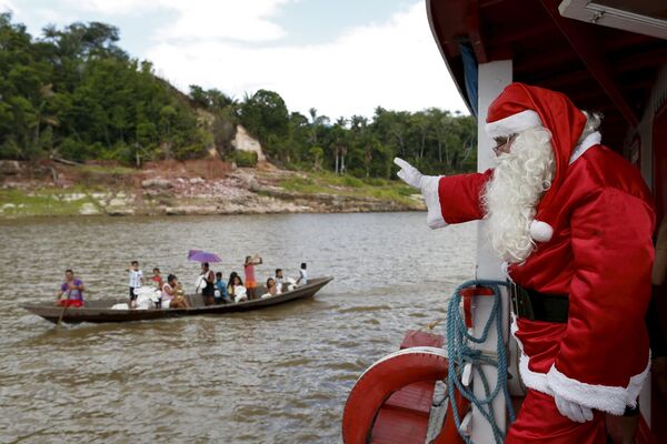 Волонтер в костюме Санта-Клауса плывет в лодке по Амазонке, Бразилия