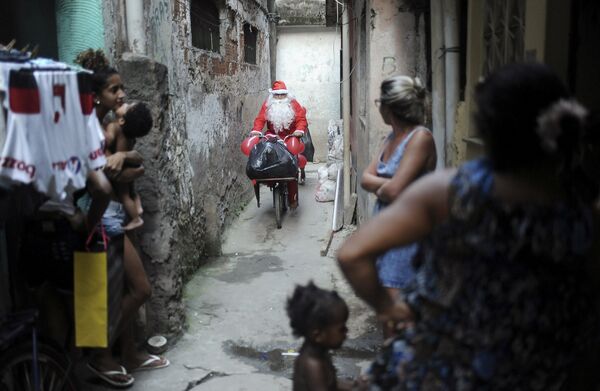 Мужчина в костюме Санта-Клауса катается на велосипеде по трущобам в Рио-де-Жанейро, Бразилия