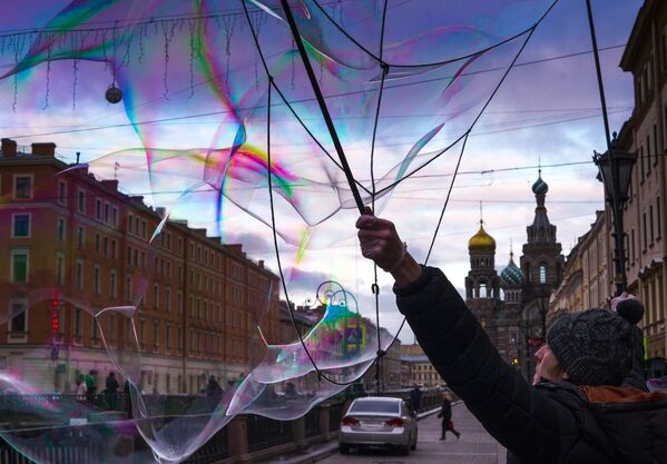 Уличный артист надувает мыльные пузыри на набережной канала Грибоедова в Санкт-Петербурге