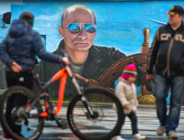 Прохожие у портрета президента России Владимира Путина на стене здания в Ялте