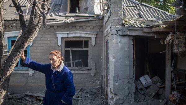 Женщина у поврежденного в результате обстрела дома в поселке Александровка Донецкой области