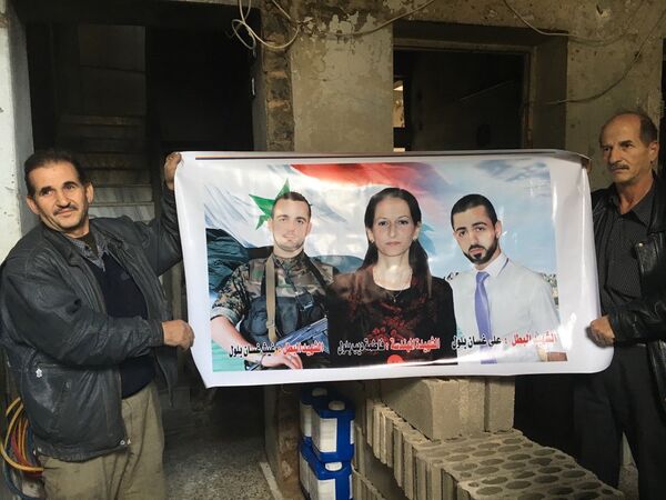 Жители Хомса показывают плакат с фотографиями родственников, погибших при тройном теракте 28 декабря в квартале аз-Захра в Хомсе в Сирии