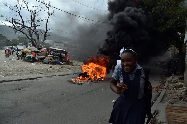 Девушка проходит мимо горящих покрышек во время акции протеста в Порт-о-Пренс, Гаити. Январь 2016