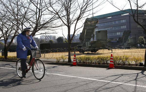 Сотрудник охраны едет на велосипеде мимо зенитно-ракетного комплекса Patriot сил самообороны Японии