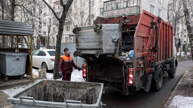 Сотрудник коммунальных служб выгружает мусор из контейнера в мусоровоз. Архивное фото