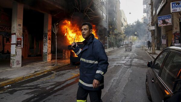 Сотрудник пожарной безопасности вызывает подкрепление во время столкновений и протестов в центре Афин, Греция. Февраль 2016