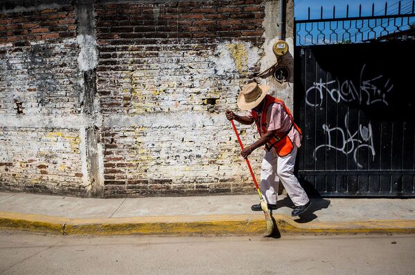 Муниципалитет работник подметает тротуар во время очистки города в Мексике