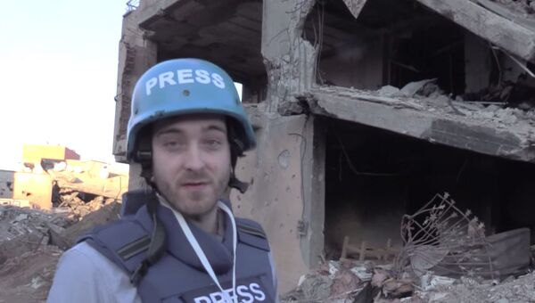 Корреспондент RT Уильям Уайтман на фоне разрушенного здания в городе Джизре