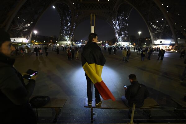 Люди возле Эйфелевой башни окрашенной в цвета бельгийского флага в память о жертвах терактов. Париж, Франция