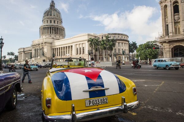 Классический американский автомобиль с изображением кубинского флага возле здания Капитолия в Гаване, Куба