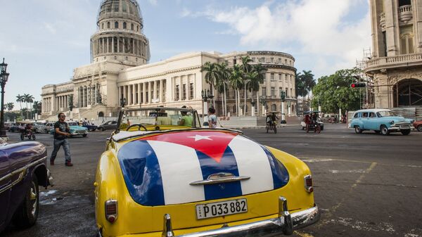 Классический американский автомобиль с изображением кубинского флага возле здания Капитолия в Гаване, Куба. Архивное фото