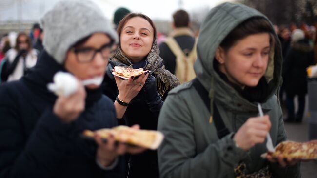 Девушки едят блины во время масленичных гуляний в Парке Горького в Москве