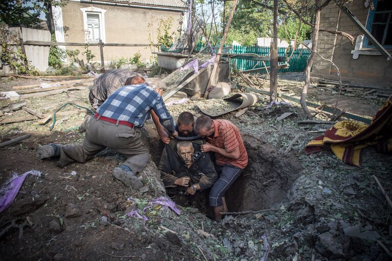 Местные жители достают из укрытия тело погибшего в результате обстрела поселка Александровка в Донецкой области