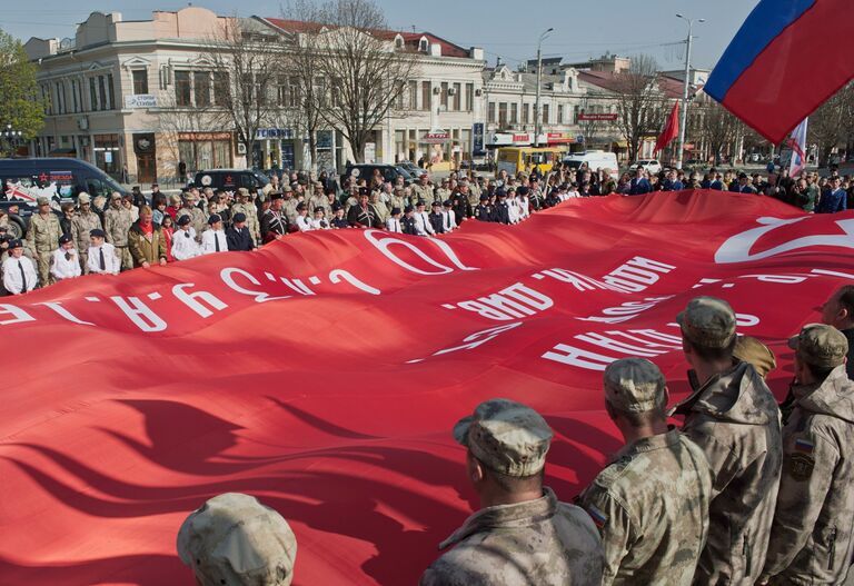 Участники митинга в Симферополе, посвященного автомаршу Звезда нашей великой Победы, разворачивают копию Знамени Победы