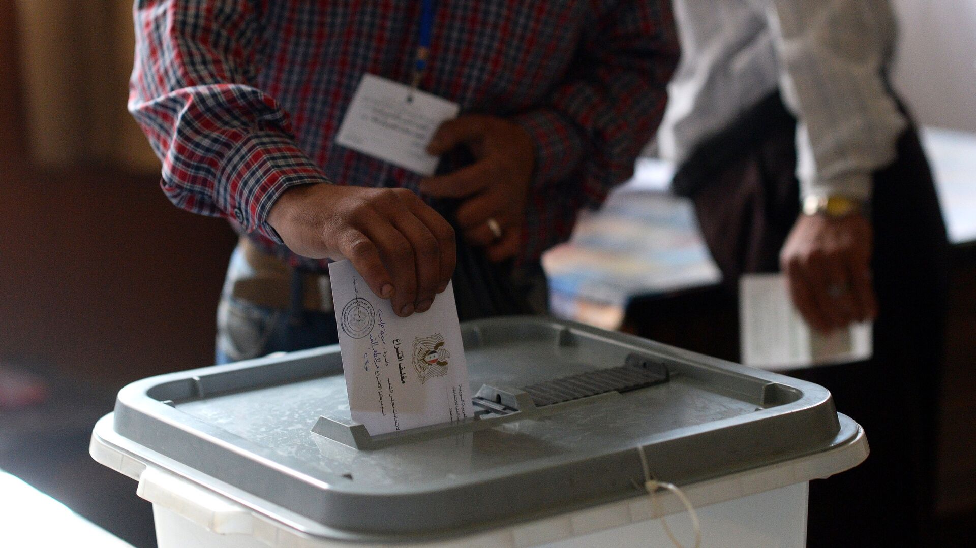Мужчина опускает конверт с бюллетенем в урну на одном из избирательных участков во время голосования на парламентских выборов в Сирии - РИА Новости, 1920, 18.04.2021