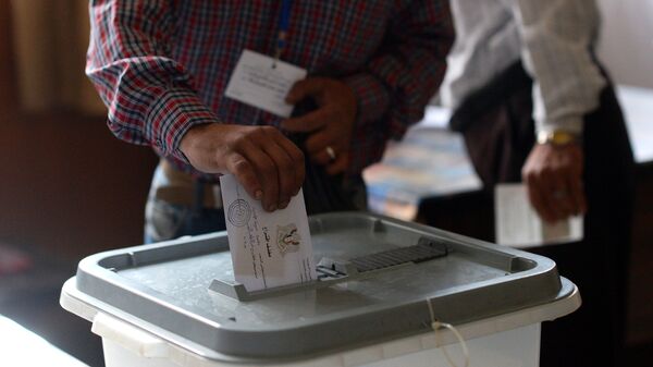 Мужчина опускает конверт с бюллетенем в урну на одном из избирательных участков во время голосования на парламентских выборов в Сирии