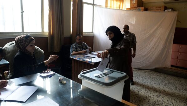 Женщина опускает конверт с бюллетенем в урну на одном из избирательных участков во время голосования на парламентских выборов в Сирии