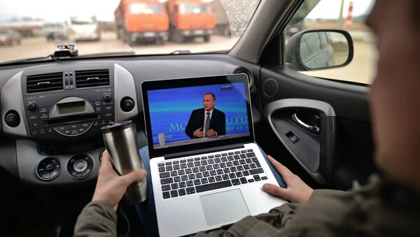 Пассажир смотрит трансляцию ежегодной специальной программы Прямая линия с Владимиром Путиным на автомобильной стоянке в Новосибирской области