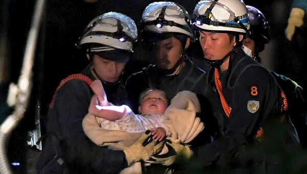 Спасатели выносят младенца из разрушенного в результате землетрясения дома. Кумамото, Япония. Апрель 2016