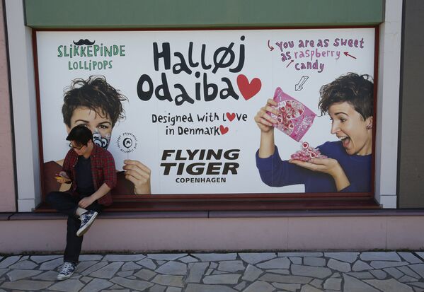 Житель у рекламного плаката конфет в районе Одайба, Токио, Япония