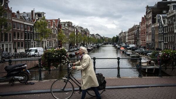 Пожилая женщина с велосипедом на мосту в центре Амстердама