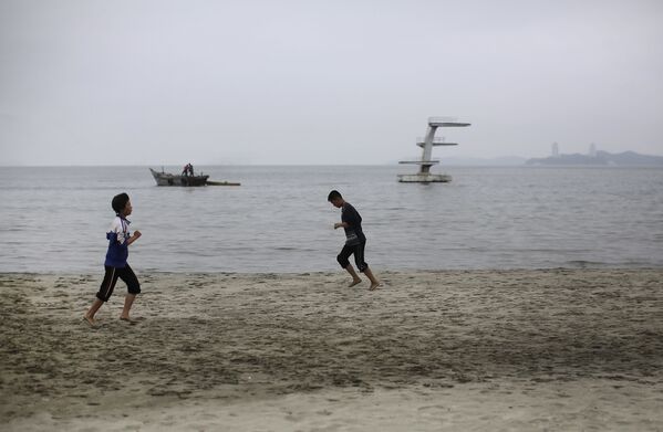 Молодые люди бегают трусцой по пляжу в Северной Корее. 21 июня 2016