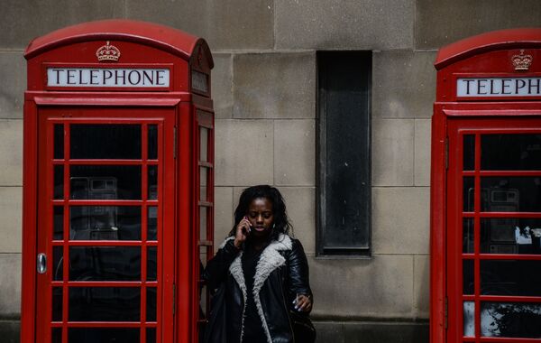Девушка разговаривает по телефону у телефонной будки в Манчестере