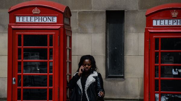 Девушка разговаривает по телефону у телефонной будки в Манчестере